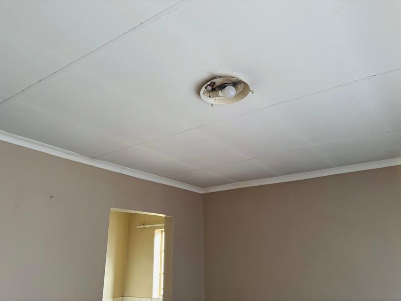 An empty room interior featuring a ceiling with a damaged light fixture and exposed wiring, requiring maintenance and cosmetic updates.