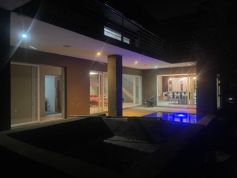 Night view of the rear exterior featuring a swimming pool, concrete patio, and sliding glass doors leading into the main living areas.