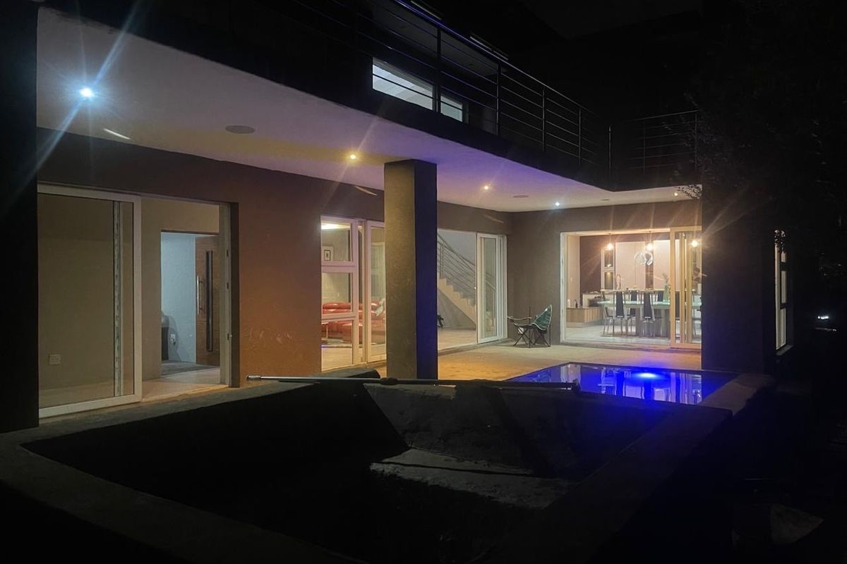 Night view of the rear exterior featuring a swimming pool, concrete patio, and sliding glass doors leading into the main living areas.