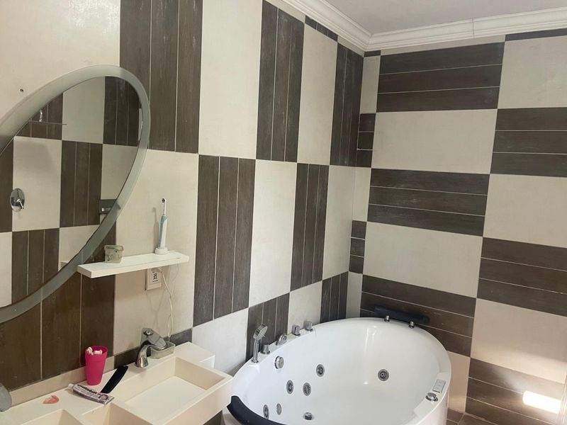 A bathroom featuring a jetted corner bathtub, wall-mounted basin, and modern two-tone tiled wall finishes.