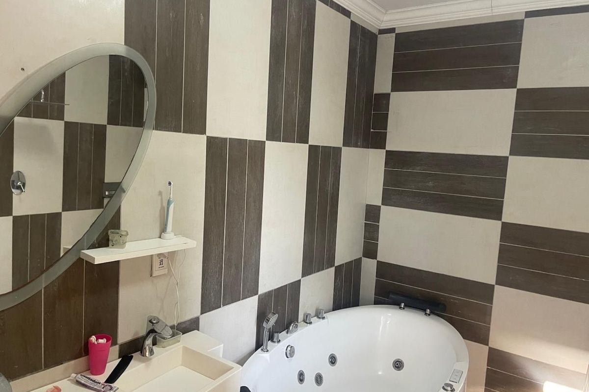 A bathroom featuring a jetted corner bathtub, wall-mounted basin, and modern two-tone tiled wall finishes.