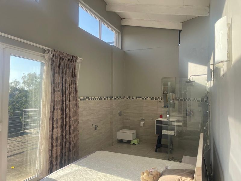 Bedroom featuring an open-plan en-suite bathroom with a walk-in shower, wall-mounted toilet, vanity, and access to a private balcony through sliding glass doors.