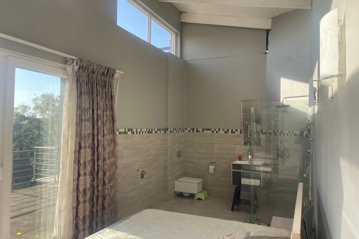 Bedroom featuring an open-plan en-suite bathroom with a walk-in shower, wall-mounted toilet, vanity, and access to a private balcony through sliding glass doors.