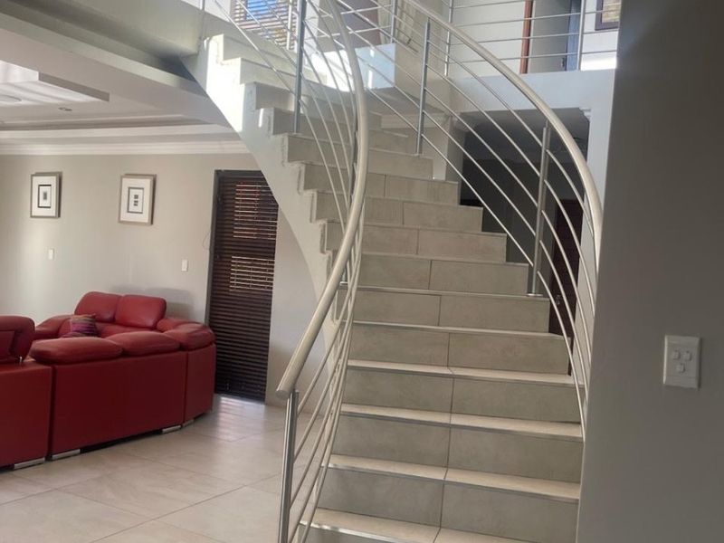 Spacious living area featuring a prominent curved staircase with stainless steel balustrades, tiled flooring, and double volume ceilings.
