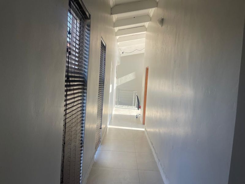 A bright, tiled hallway featuring exposed ceiling beams and venetian blinds, providing a clean, neutral transition space between rooms.