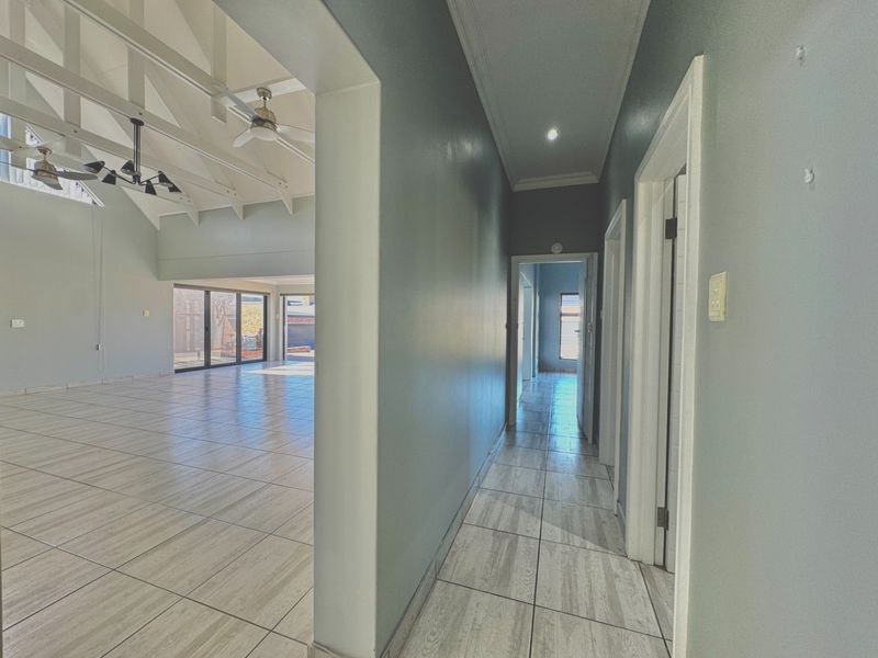 A spacious, empty hallway with tiled flooring and vaulted ceilings, leading into an open-plan living area with large sliding glass doors.