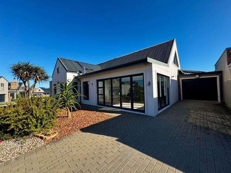 Modern single-story residence featuring a corrugated metal roof, paved driveway, and large aluminium-framed sliding doors leading into the main living area.