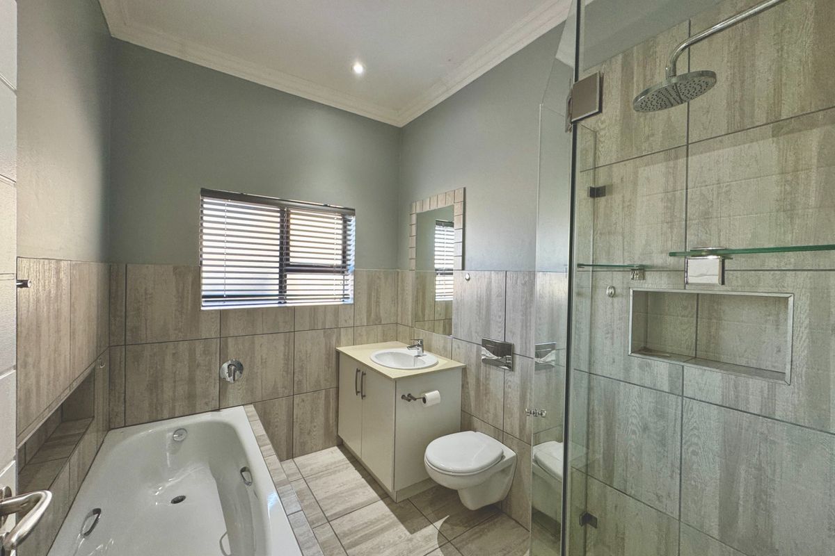 Modern bathroom featuring a built-in bathtub, a glass-enclosed shower with a recessed niche, a wall-mounted toilet, and a vanity cabinet with neutral tiling.