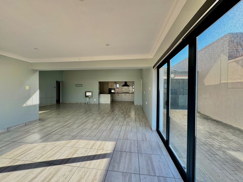 Spacious open-plan living area featuring modern tiled flooring, large sliding glass doors leading to the exterior, and a view into the kitchen.