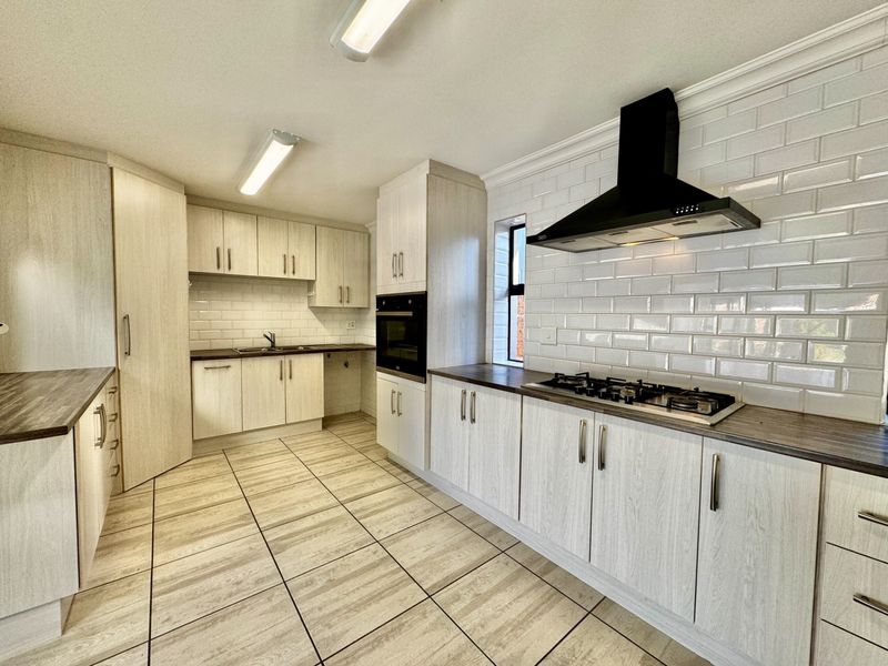 Modern kitchen featuring light wood-grain cabinetry, dark laminate countertops, subway tile backsplash, gas hob, built-in oven, and tiled flooring.