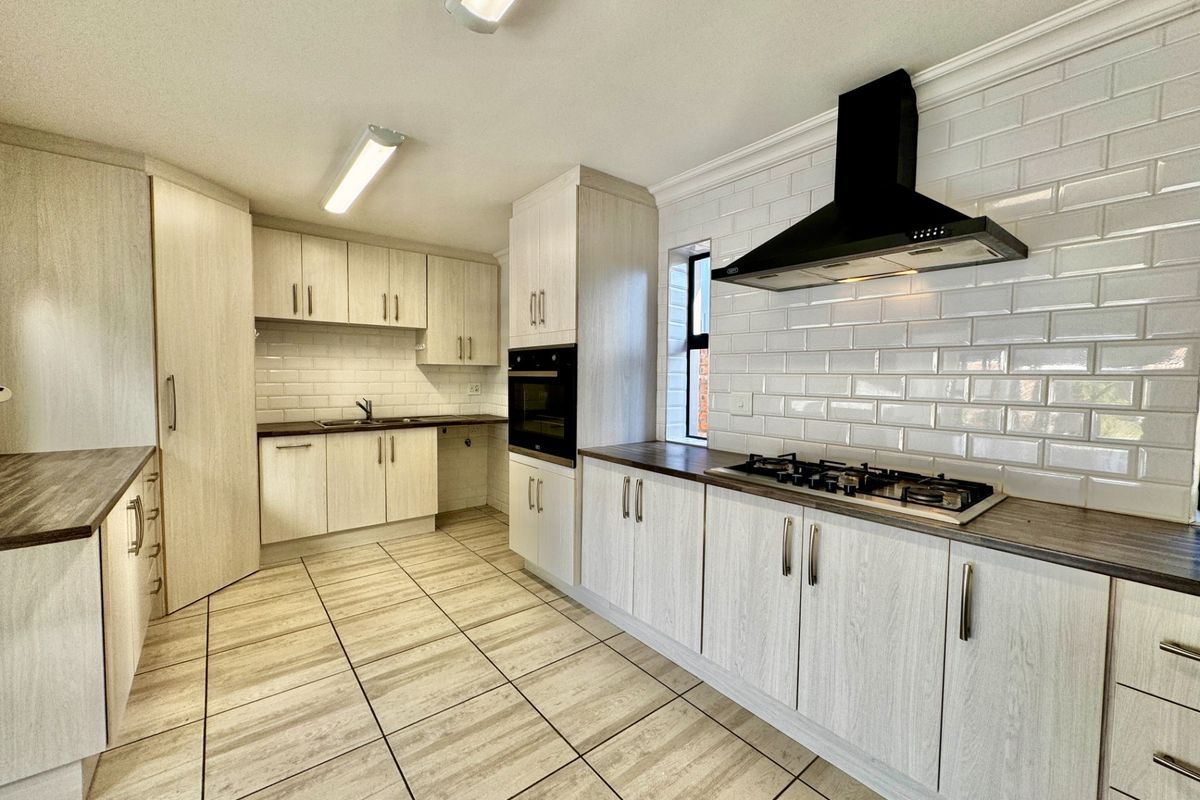 Modern kitchen featuring light wood-grain cabinetry, dark laminate countertops, subway tile backsplash, gas hob, built-in oven, and tiled flooring.