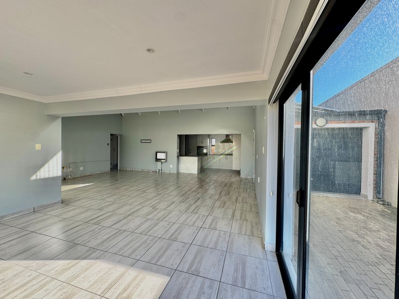 Spacious open-plan living and kitchen area featuring modern tiled flooring, recessed lighting, and large sliding doors leading to an outdoor patio space.