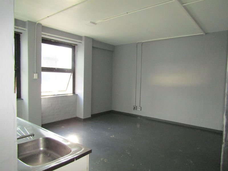 An empty kitchen area featuring a stainless steel sink, exposed electrical conduit, and a window, offering a blank canvas for renovation.