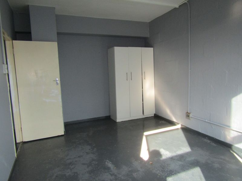 A simple, empty bedroom featuring painted concrete flooring, a built-in wardrobe, and exposed electrical conduit along the wall.