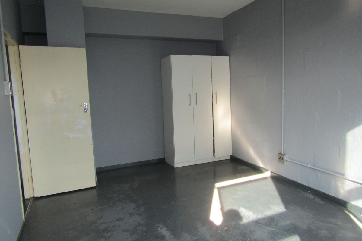 A simple, empty bedroom featuring painted concrete flooring, a built-in wardrobe, and exposed electrical conduit along the wall.