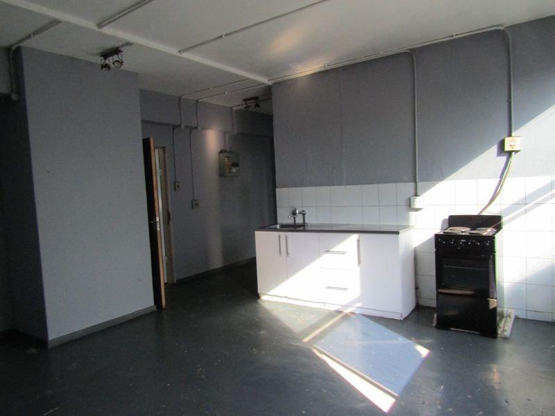 A basic, empty kitchen area featuring white cabinetry, a stainless steel sink, and an electric stove with exposed electrical conduit and tiled splashback.