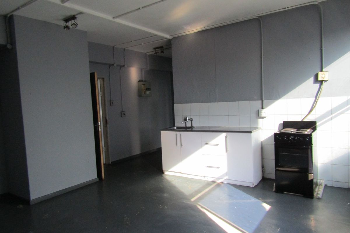A basic, empty kitchen area featuring white cabinetry, a stainless steel sink, and an electric stove with exposed electrical conduit and tiled splashback.
