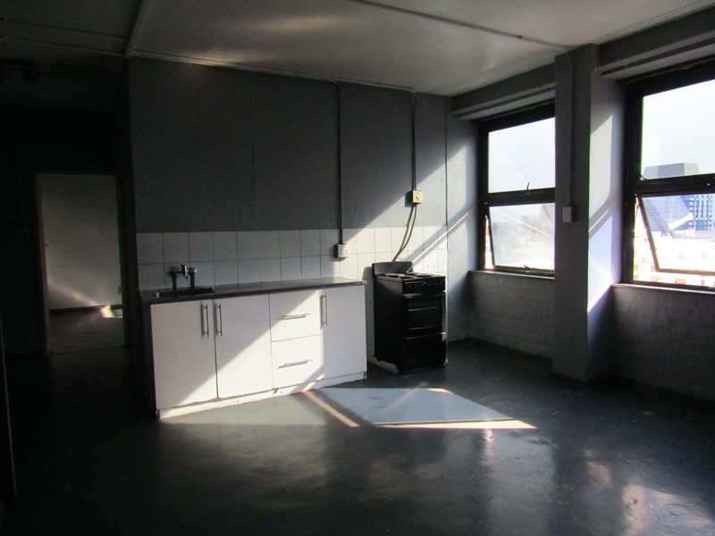 An empty kitchen area featuring basic cabinetry, a sink, and a standalone stove, with large windows providing natural light.