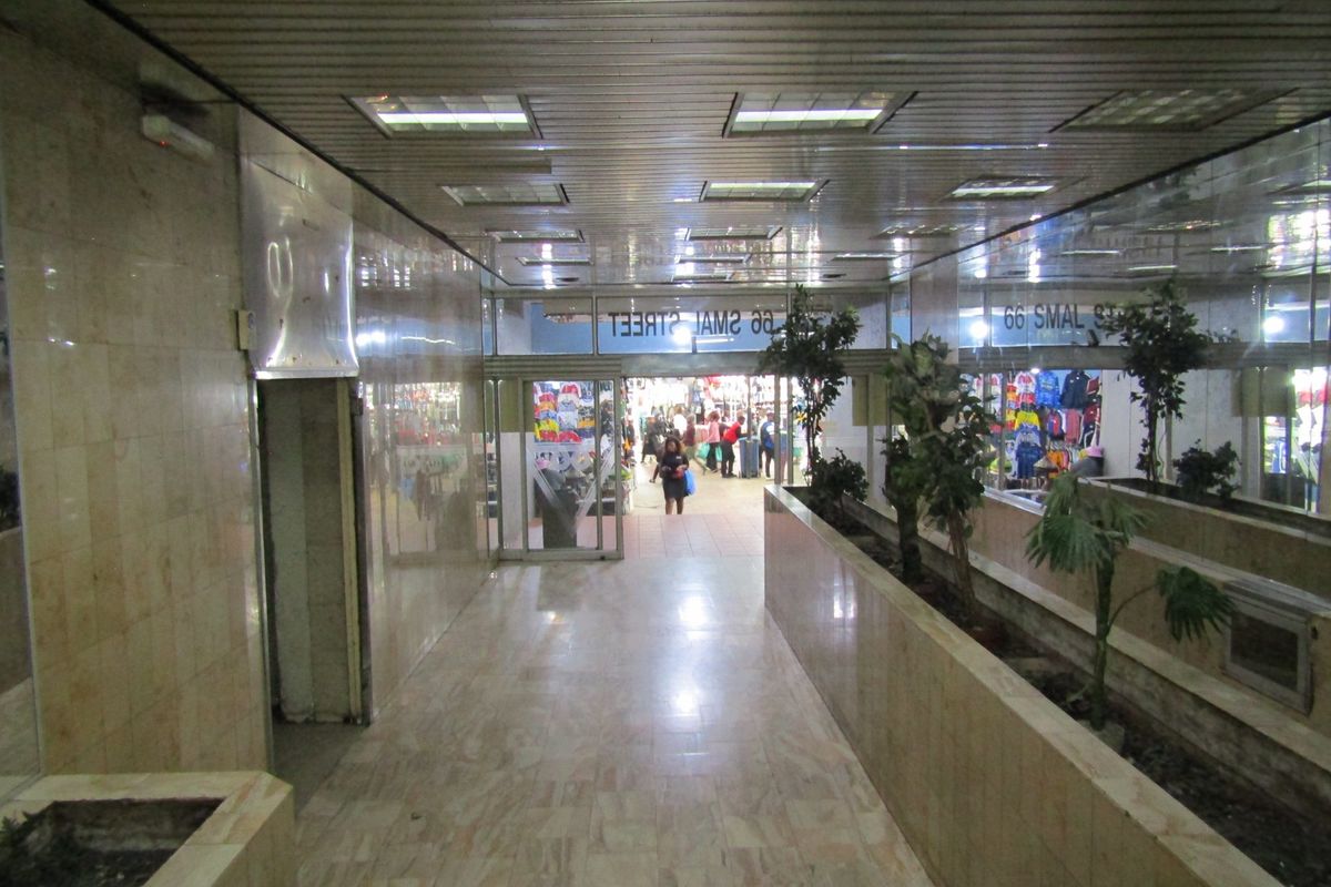 A spacious commercial hallway featuring marble wall and floor finishes, recessed ceiling lighting, and integrated planter boxes leading to a street-level entrance.