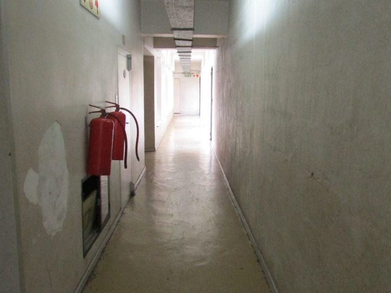A utilitarian apartment hallway featuring exposed cable trays, fire safety equipment, and plain wall finishes.