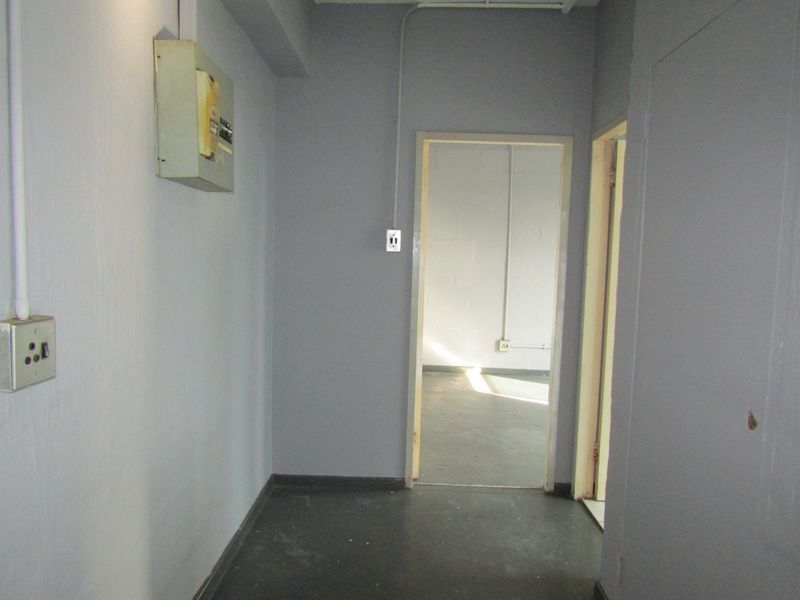 A functional hallway featuring exposed electrical conduit and a wall-mounted distribution board, leading into an adjacent room.