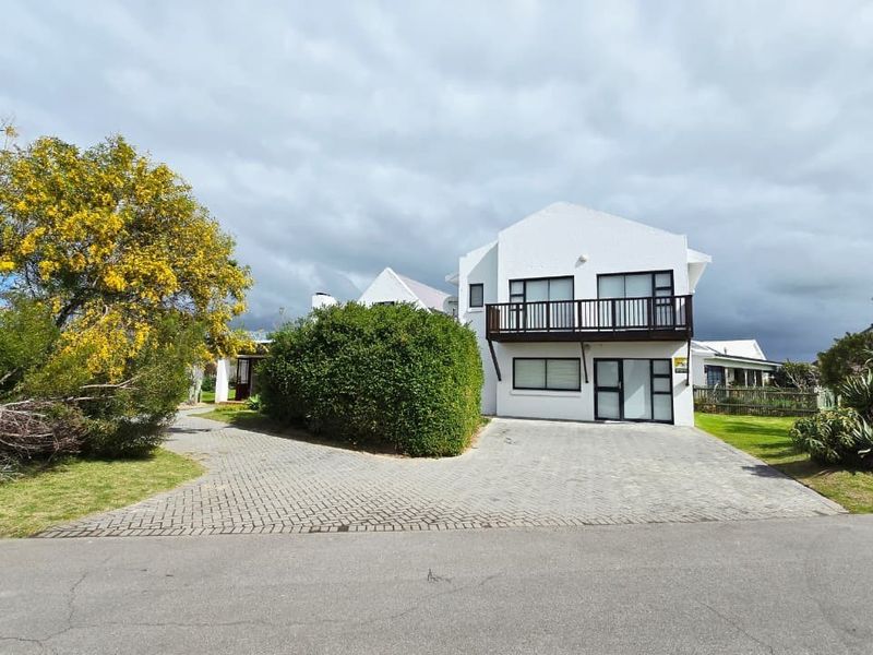 Front view of a two-story residential property featuring a paved driveway, white facade, and an upper-level balcony with metal railings.