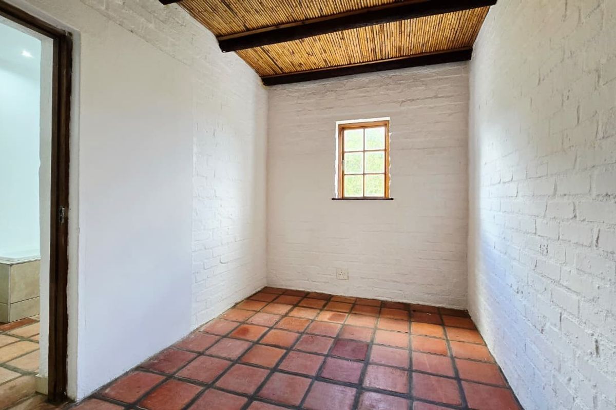 An empty bedroom featuring white-painted exposed brick walls, a unique bamboo ceiling, and traditional terracotta floor tiles, with an adjacent bathroom visible.