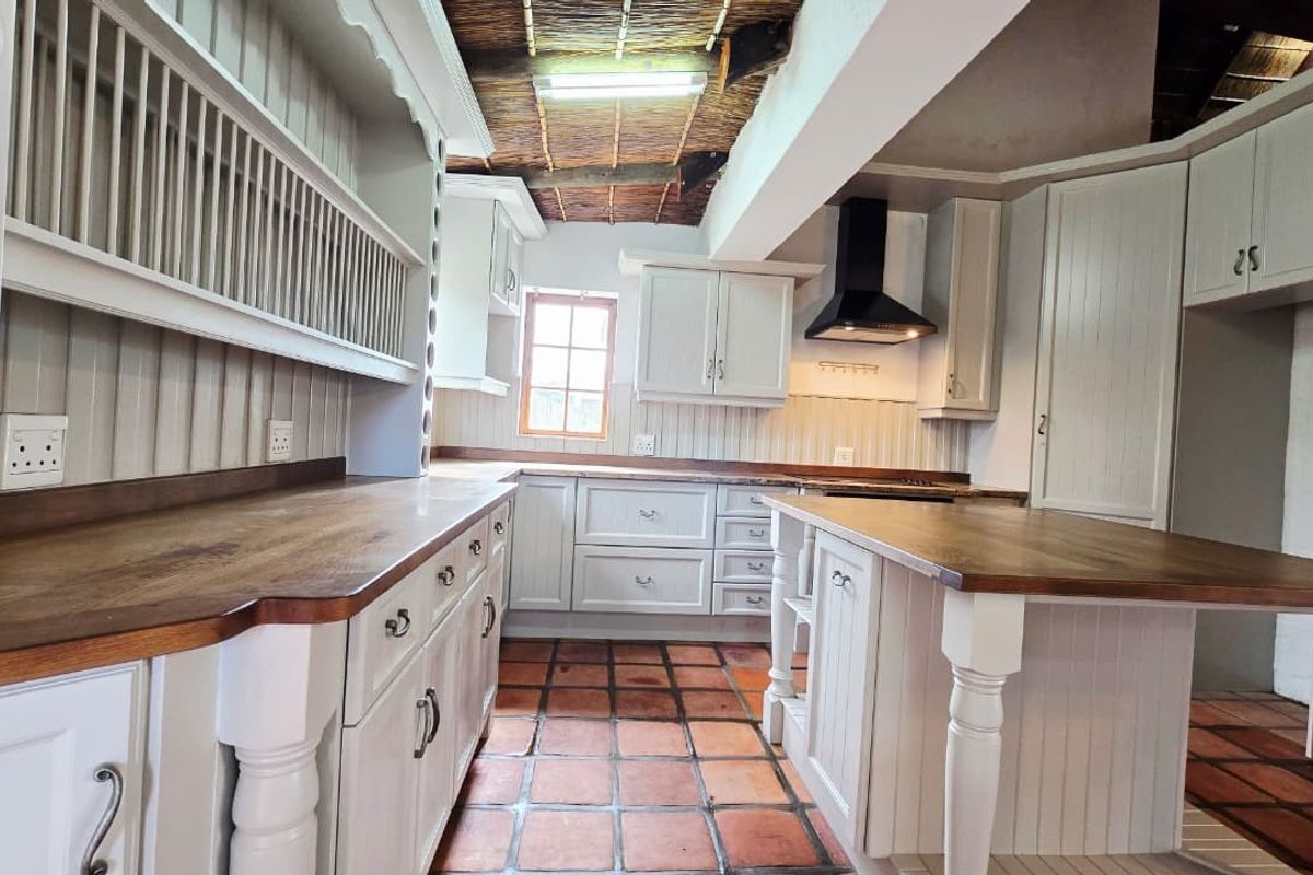 A rustic kitchen featuring white cabinetry, wooden countertops, terracotta flooring, and a unique exposed thatch ceiling with an integrated extractor fan.