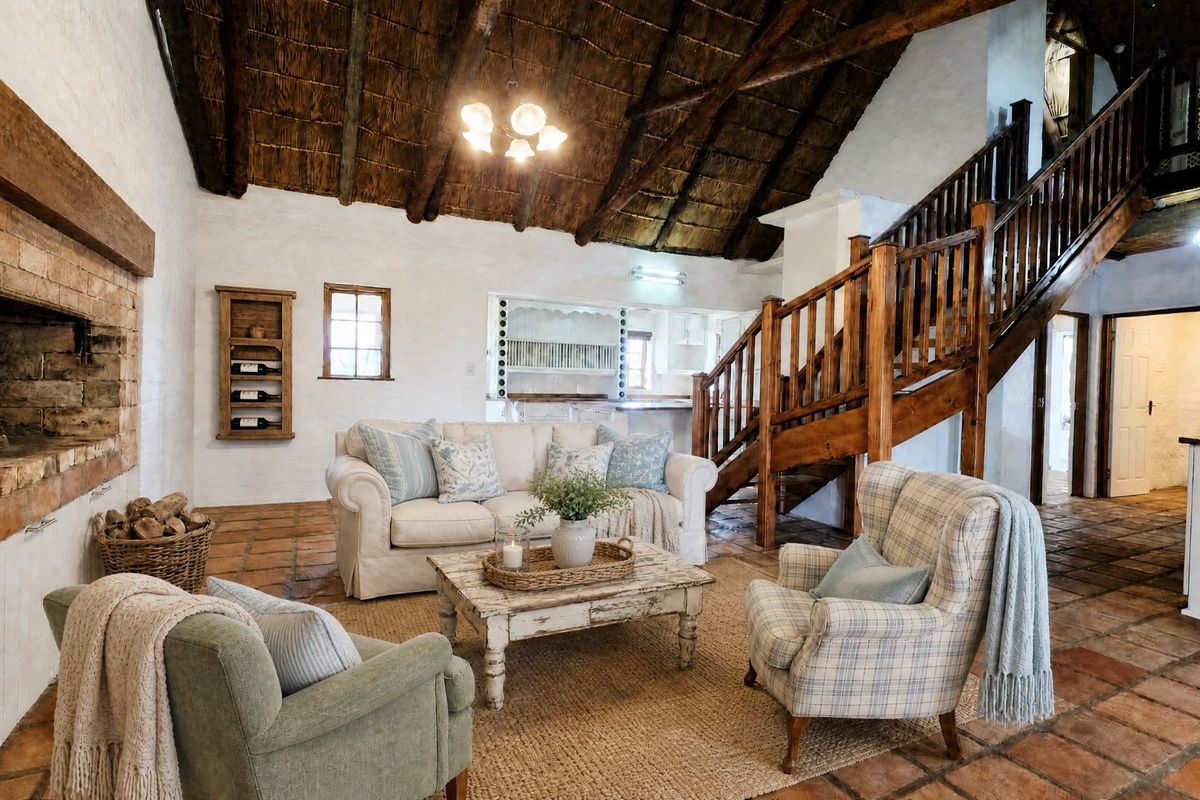 Spacious living room featuring a high thatched ceiling with exposed timber rafters, a rustic brick fireplace, and traditional terracotta floor tiles.