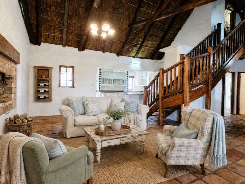 Spacious living room featuring a high thatched ceiling with exposed timber rafters, a rustic brick fireplace, and traditional terracotta floor tiles.