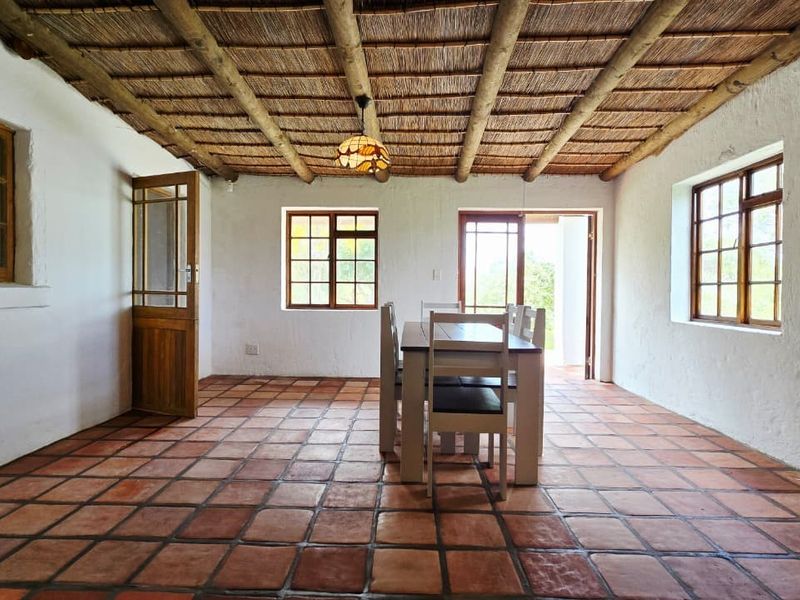 Dining room featuring a rustic thatched ceiling with exposed timber beams, terracotta tile flooring, and multiple timber-framed windows and doors.