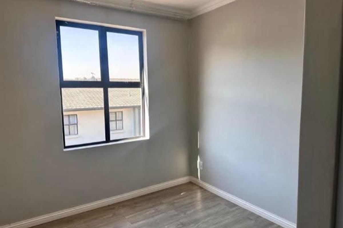 A clean, empty bedroom featuring modern grey laminate flooring, neutral walls, and a large aluminium-framed window providing natural light.