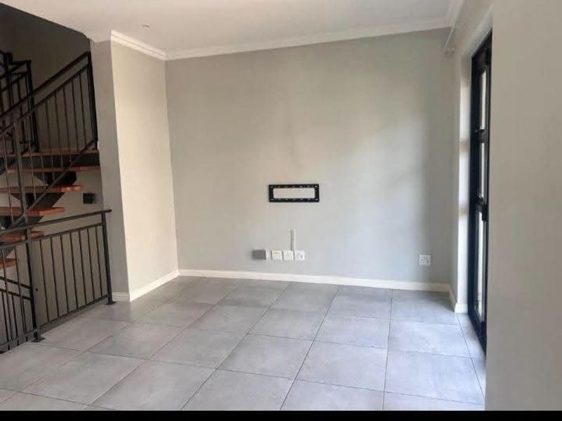 An empty, modern living area featuring neutral tiled flooring, a staircase with a metal balustrade, and a wall-mounted TV bracket.