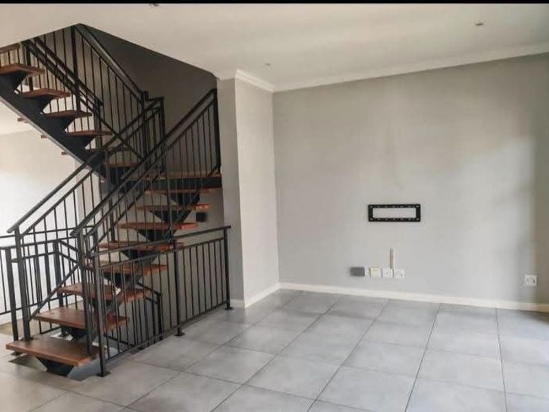 An open-plan living area featuring a modern open-tread staircase with a black metal balustrade and neutral tiled flooring throughout.