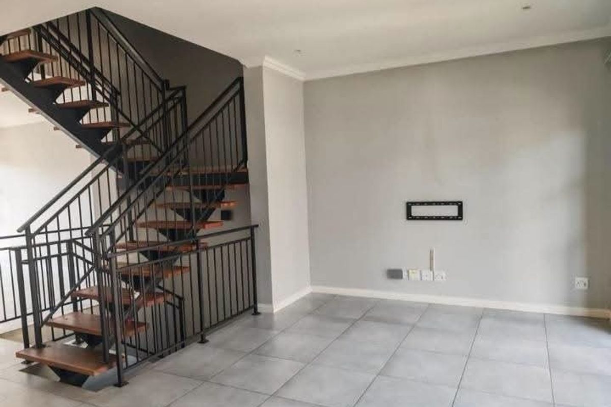 An open-plan living area featuring a modern open-tread staircase with a black metal balustrade and neutral tiled flooring throughout.