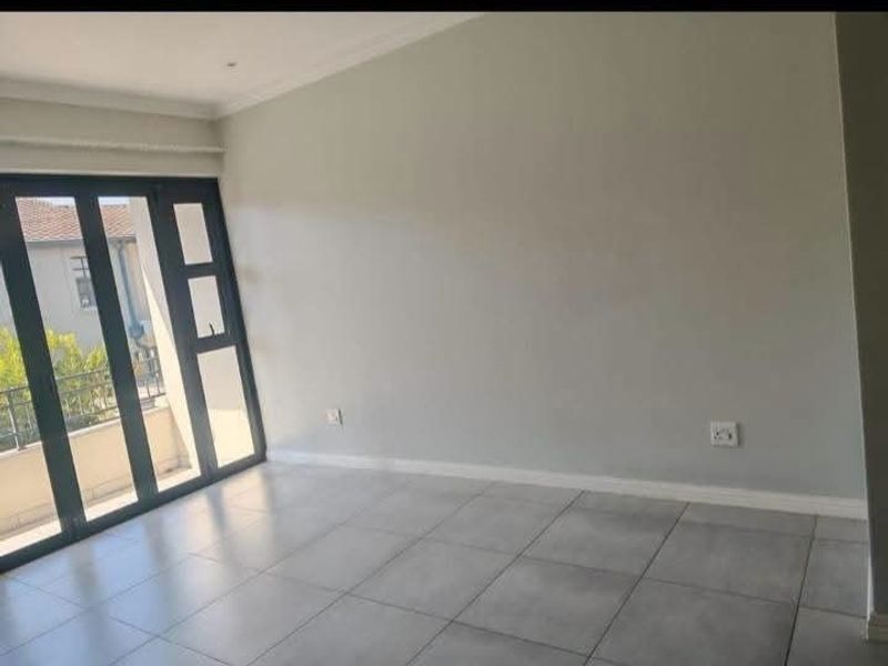 A bright, empty living area featuring neutral tiled flooring and large aluminium-framed glass doors that provide ample natural light and access to the exterior.