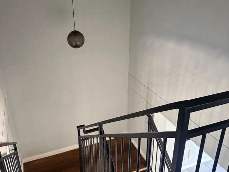 A modern staircase featuring timber treads and a sleek black metal balustrade, illuminated by a contemporary pendant light.