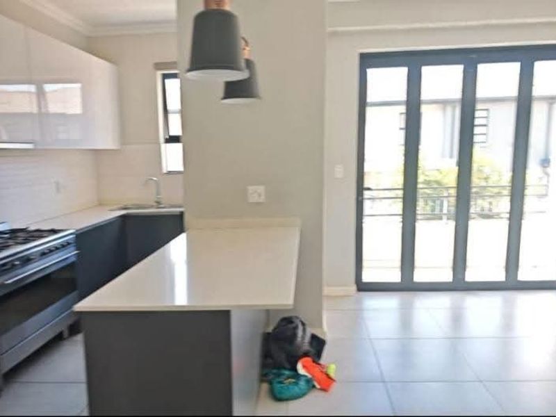 Modern open-plan kitchen featuring stone countertops, built-in cabinetry, and a gas stove, flowing seamlessly through folding glass doors to the outdoor area.
