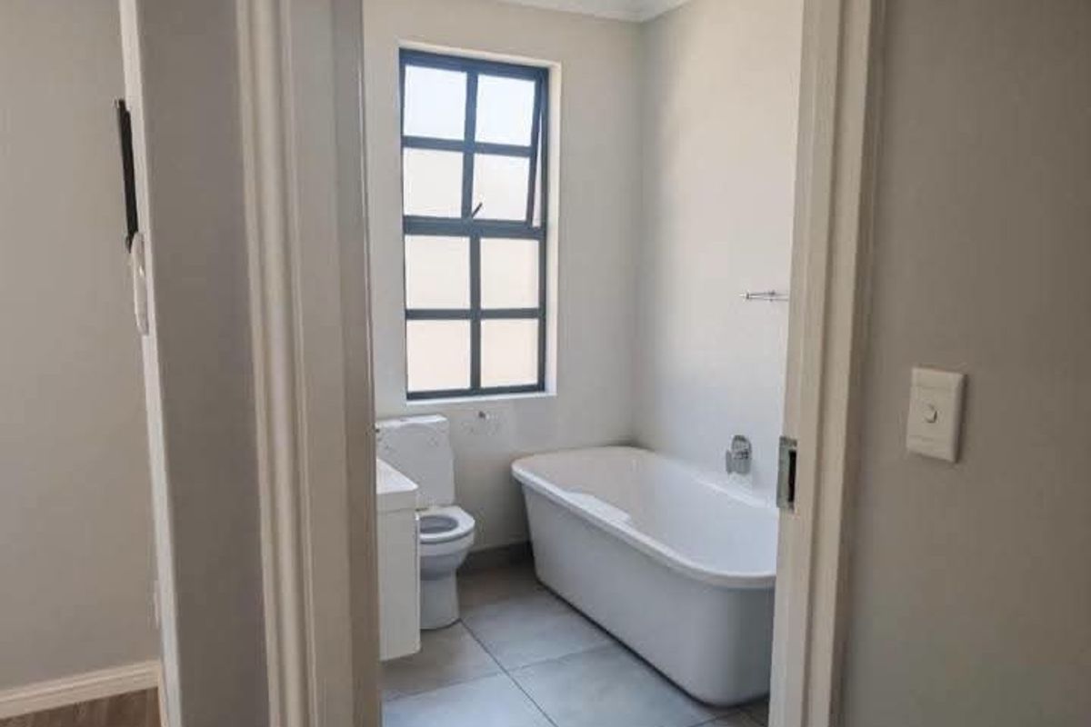 A clean, modern bathroom featuring a freestanding bathtub, a vanity basin, and a toilet with neutral tiled flooring and natural light.