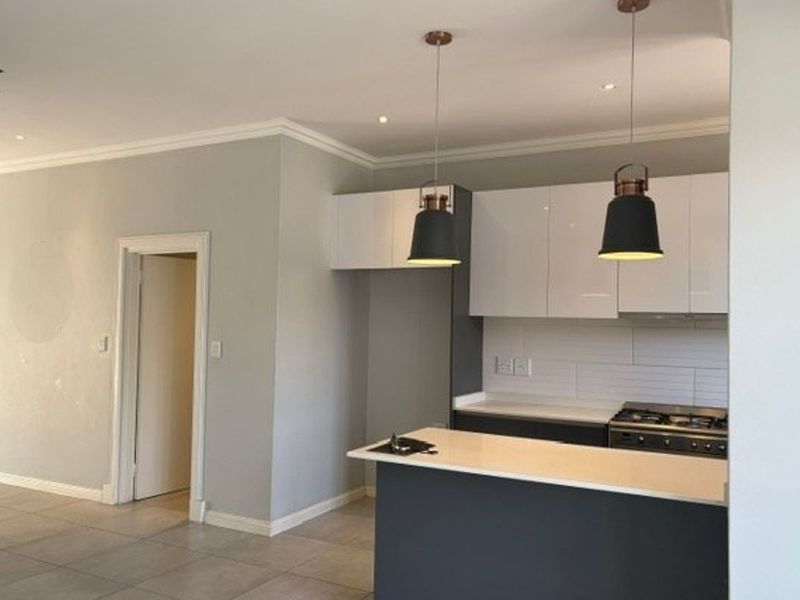 Modern kitchen featuring sleek white and dark cabinetry, stone countertops, gas hob, oven, and stylish pendant lighting, set against a neutral tiled floor.