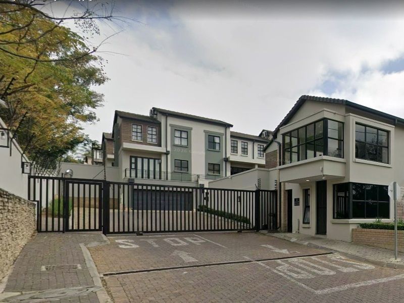 Front entrance view of a secure residential complex featuring a gated access point, guard house, and paved driveway.