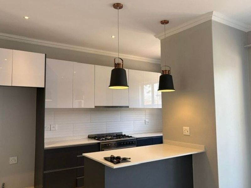 Modern kitchen featuring sleek white and dark cabinetry, stone countertops, gas hob, extractor fan, and stylish pendant lighting.