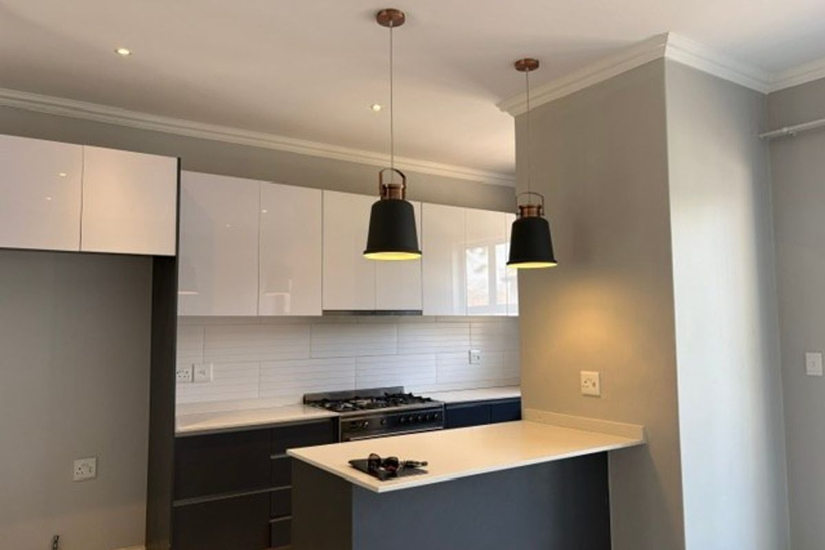 Modern kitchen featuring sleek white and dark cabinetry, stone countertops, gas hob, extractor fan, and stylish pendant lighting.