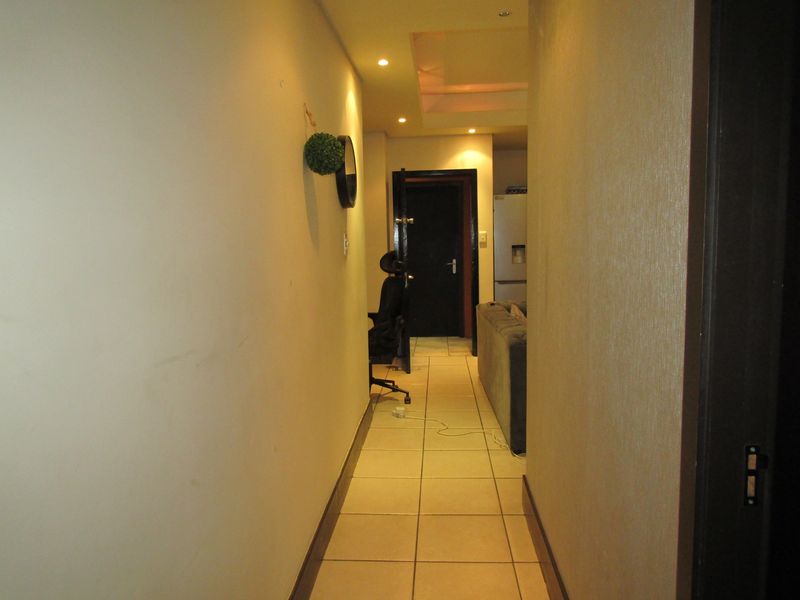 A narrow hallway featuring tiled flooring and recessed ceiling lighting, providing access to adjacent rooms within the apartment.