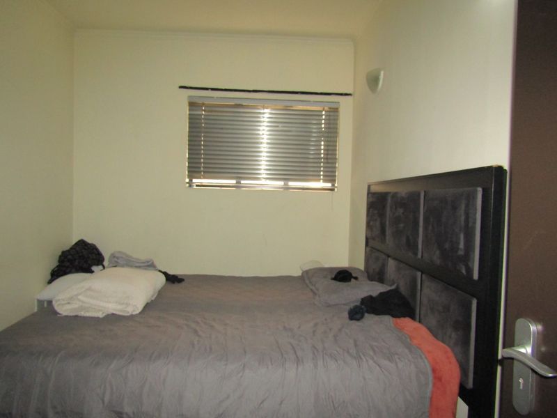 A standard bedroom featuring a window with venetian blinds and a wall-mounted light fixture.