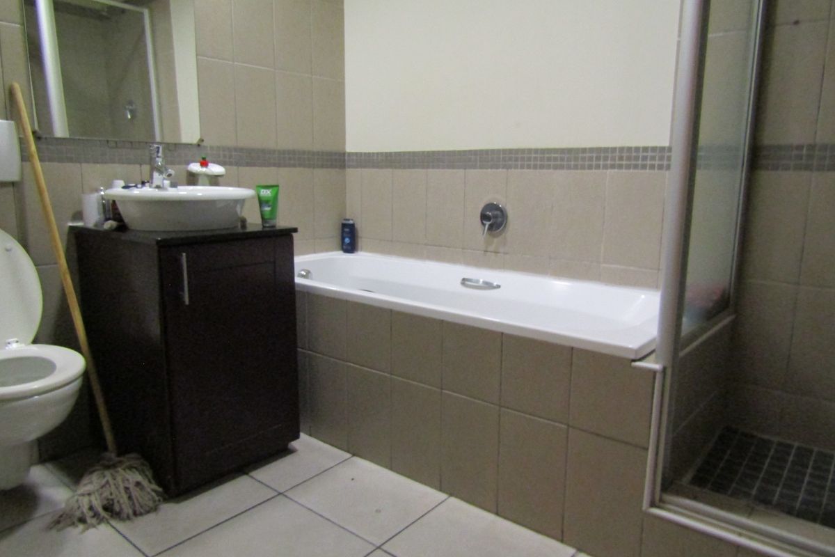 A functional bathroom featuring a vanity basin, bathtub, and separate shower enclosure with neutral wall and floor tiling.