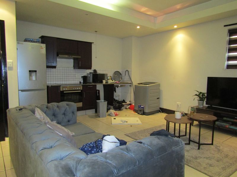 Open-plan living area featuring a compact kitchen with dark cabinetry, tiled flooring, and recessed lighting, requiring minor repairs to cabinetry and finishes.