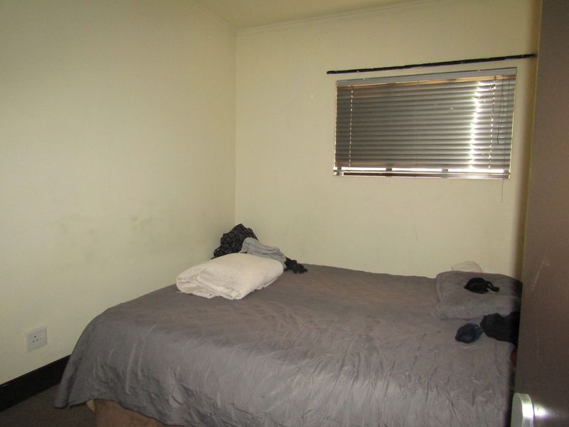 A compact bedroom featuring neutral walls, a window with venetian blinds, and an electrical outlet.