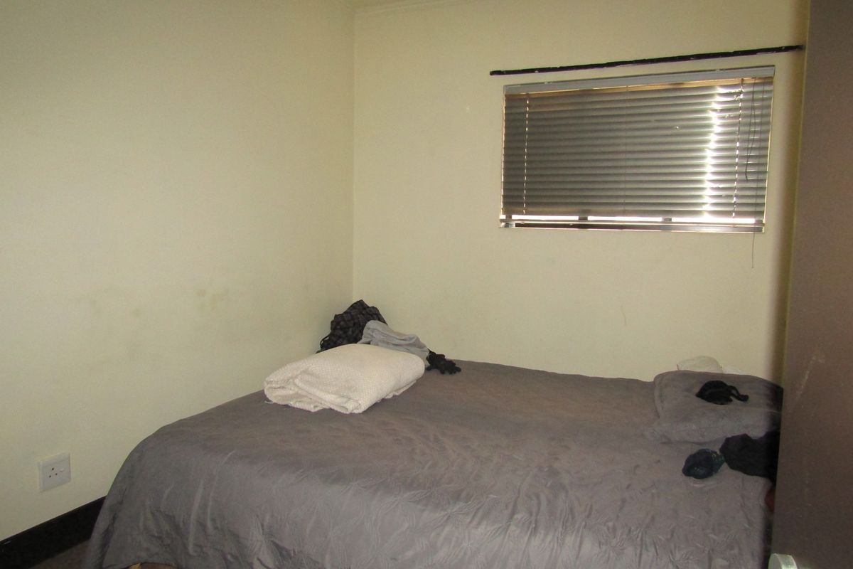 A compact bedroom featuring neutral walls, a window with venetian blinds, and an electrical outlet.