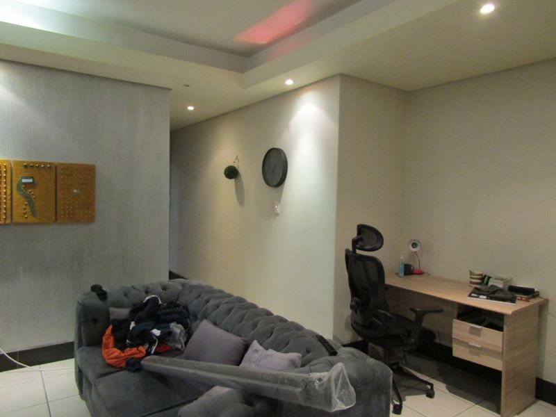 A living area featuring recessed ceiling lighting and tiled flooring, currently utilized as a multi-functional space with a desk and seating.